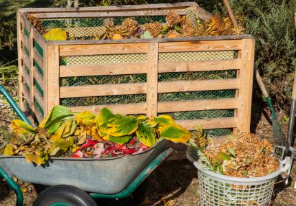 Community compost bin with wheelbarrow and laundry basket of landscape trimmings and food scraps in front