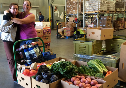 Food recovery organization volunteers stand hugging behind a cart of fresh food