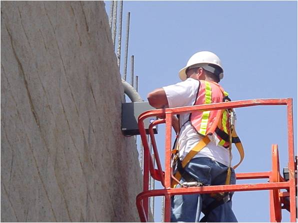 Construction worker on a lift installing tilt meter at top of concrete wall.