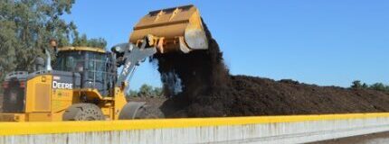 Backhoe putting compost into bay