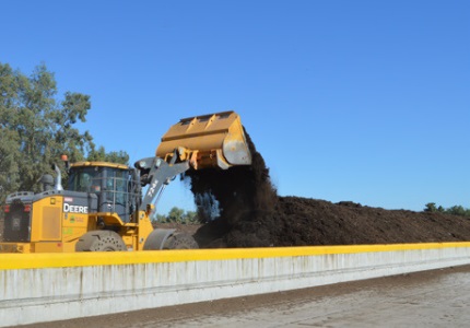 Backhoe putting compost into bay