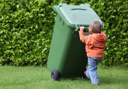 A young boy pushes an organics curbside bin across the grass
