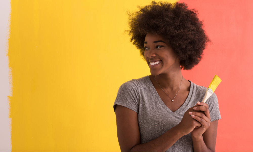 Person holding paint brush in front of vibrantly colored wall