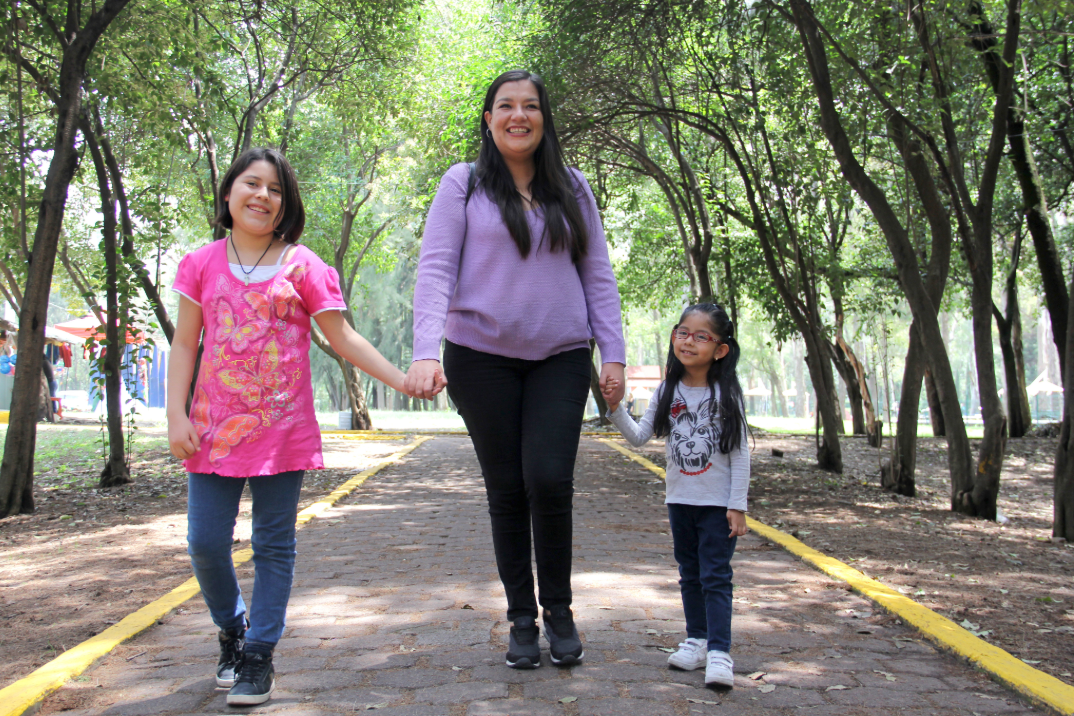 Mother and two daughters under a park tree canopy.