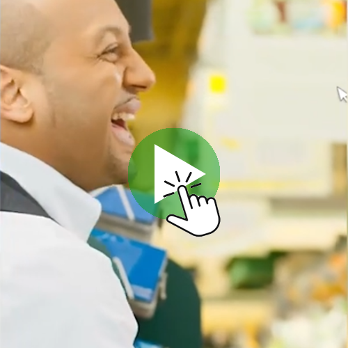 A person standing in front of a display, with a large green play‑button icon and a hand‑cursor graphic overlaid in the center. Persona observando productos en un entorno interior, con un ícono de botón de reproducción y un cursor superpuesto al centro.